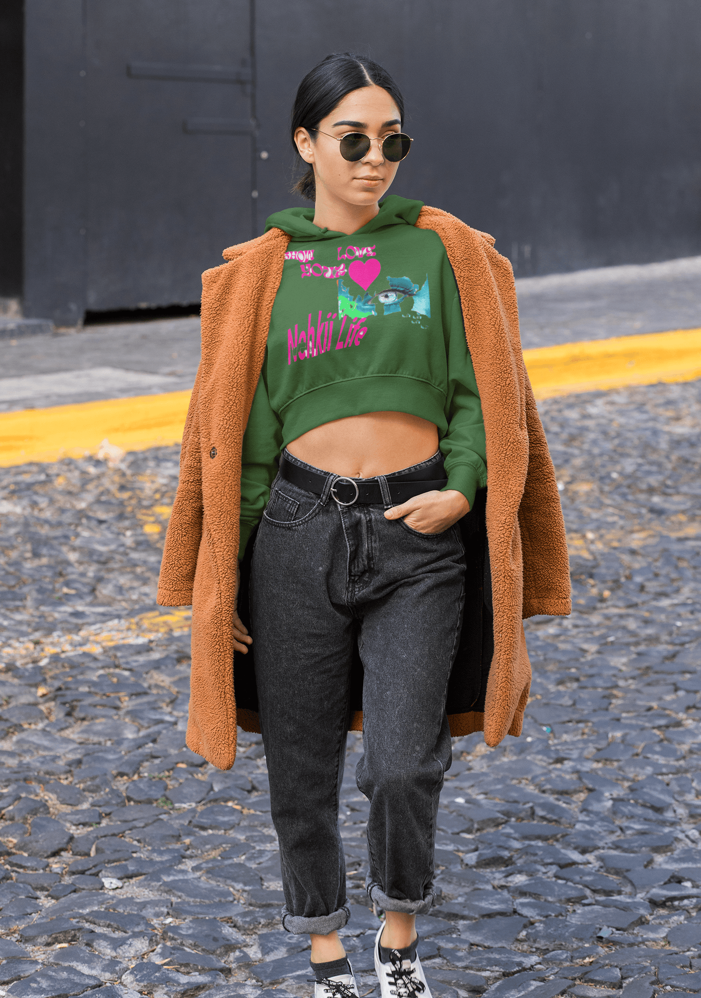 Green eco-friendly cropped hoodie with colorful design, styled with a brown coat for a trendy and sustainable women's outfit.