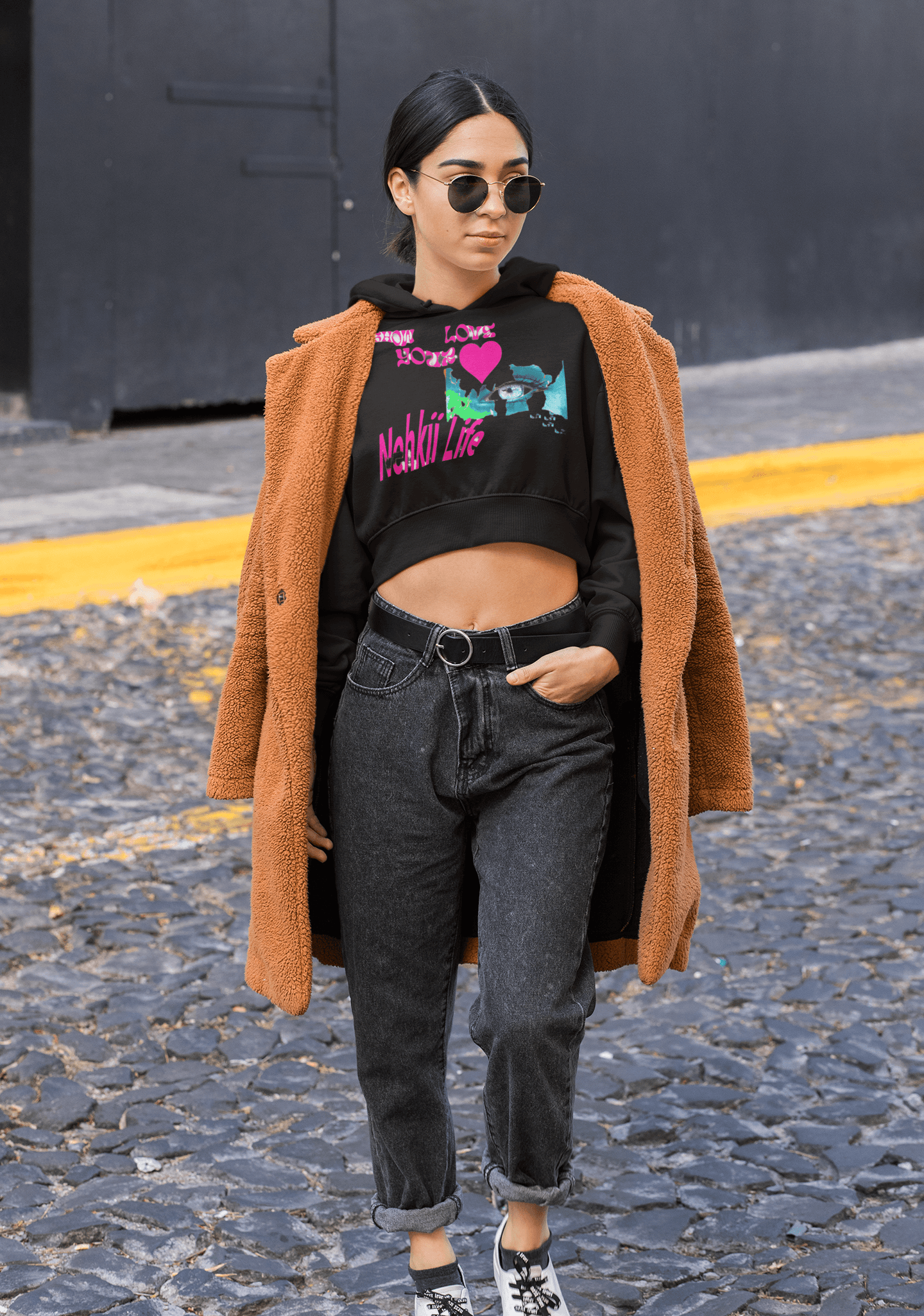 Black eco-conscious cropped hoodie with bright graphic, paired with a brown coat for a stylish and sustainable women's fashion statement.